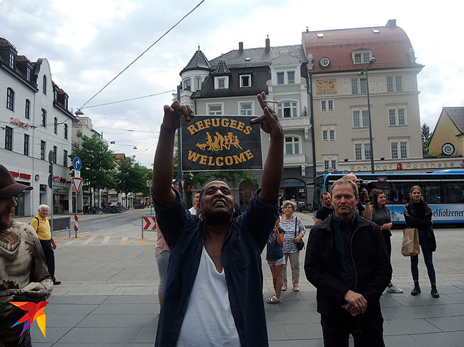 «Добро пожаловать, беженцы» - плакат с этой надписью держит довольный смуглокожий мигрант в Мюнхене. Многие немцы его радость не разделяют. Фото: Дарья АСЛАМОВА