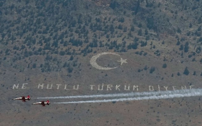 Турецкие пилотажные самолеты пролетают перед гигантским турецким флагом с надписью на турецком языке «Как счастлив тот, кто говорит, что я турок» на горе Пентадахтилос во время военного парада, посвященного 48-й годовщине турецкого вторжения 1974 года.